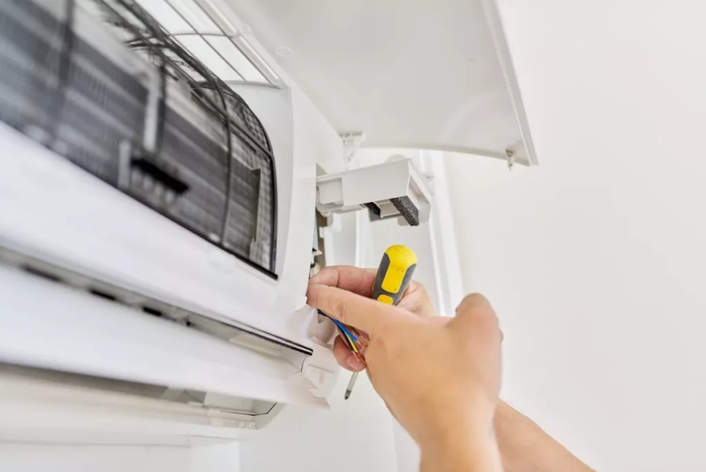 Close-up of an HVAC technician using a screwdriver to service internal wiring of a wall-mounted air conditioning unit.