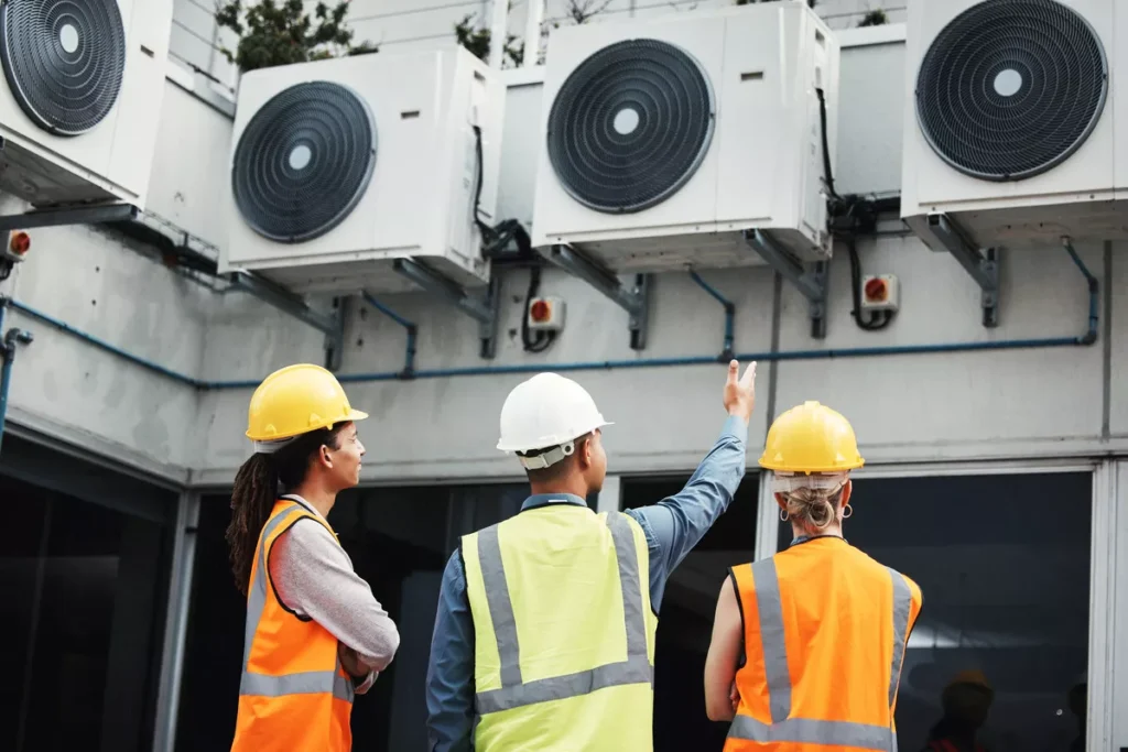 A team of three HVAC specialists in safety vests and hard hats conducting a group inspection of large-scale commercial AC units in Aurora.