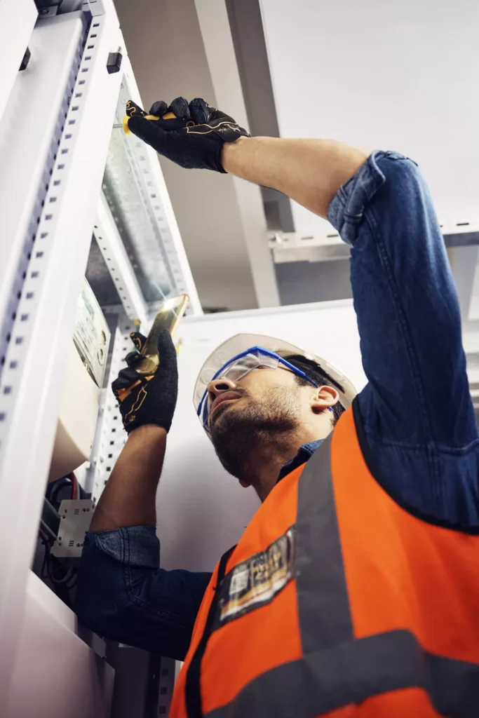 A specialized HVAC technician in full safety gear, including a hard hat and safety glasses, repairing a commercial electrical control panel in Aurora.