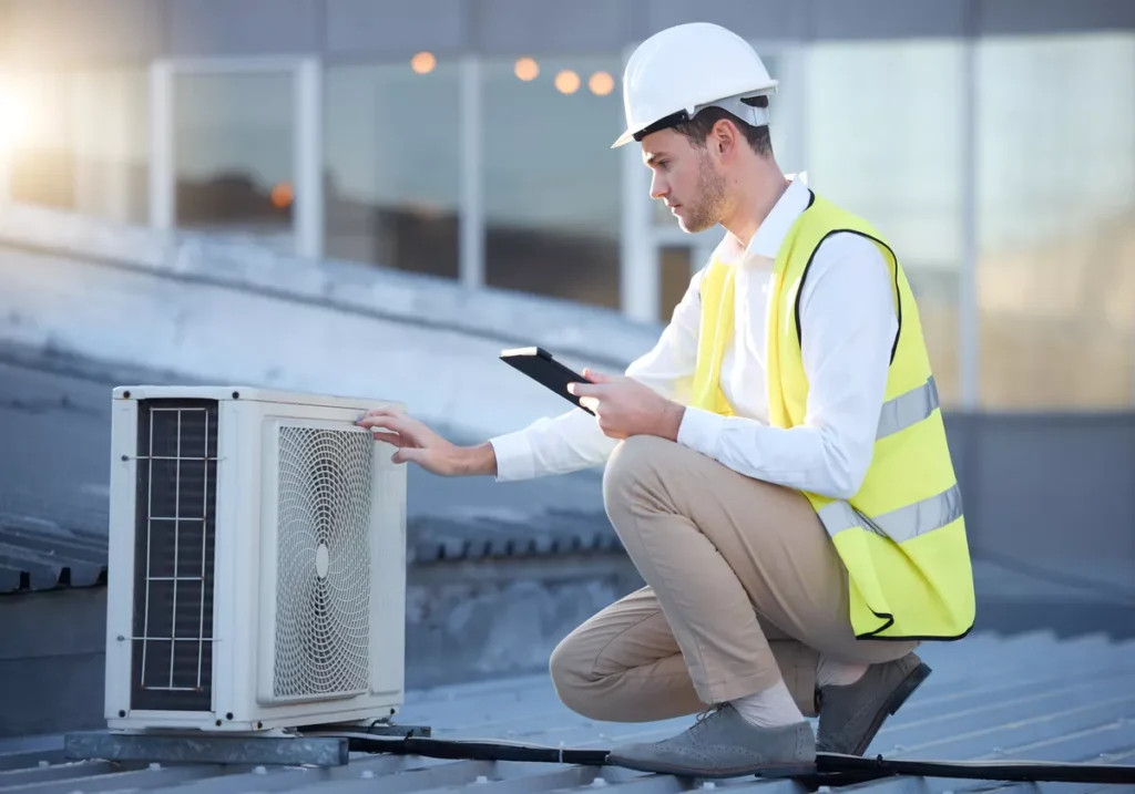A lead HVAC technician in a white hard hat and safety vest using a digital tablet to run diagnostics on a rooftop unit in Aurora.