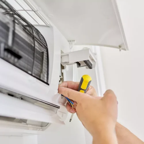 Close-up of an HVAC technician using a screwdriver to service internal wiring of a wall-mounted air conditioning unit.
