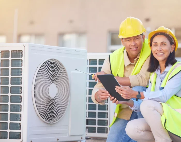 A professional male and female HVAC team in Aurora using a tablet and tools to inspect rooftop air conditioning units.
